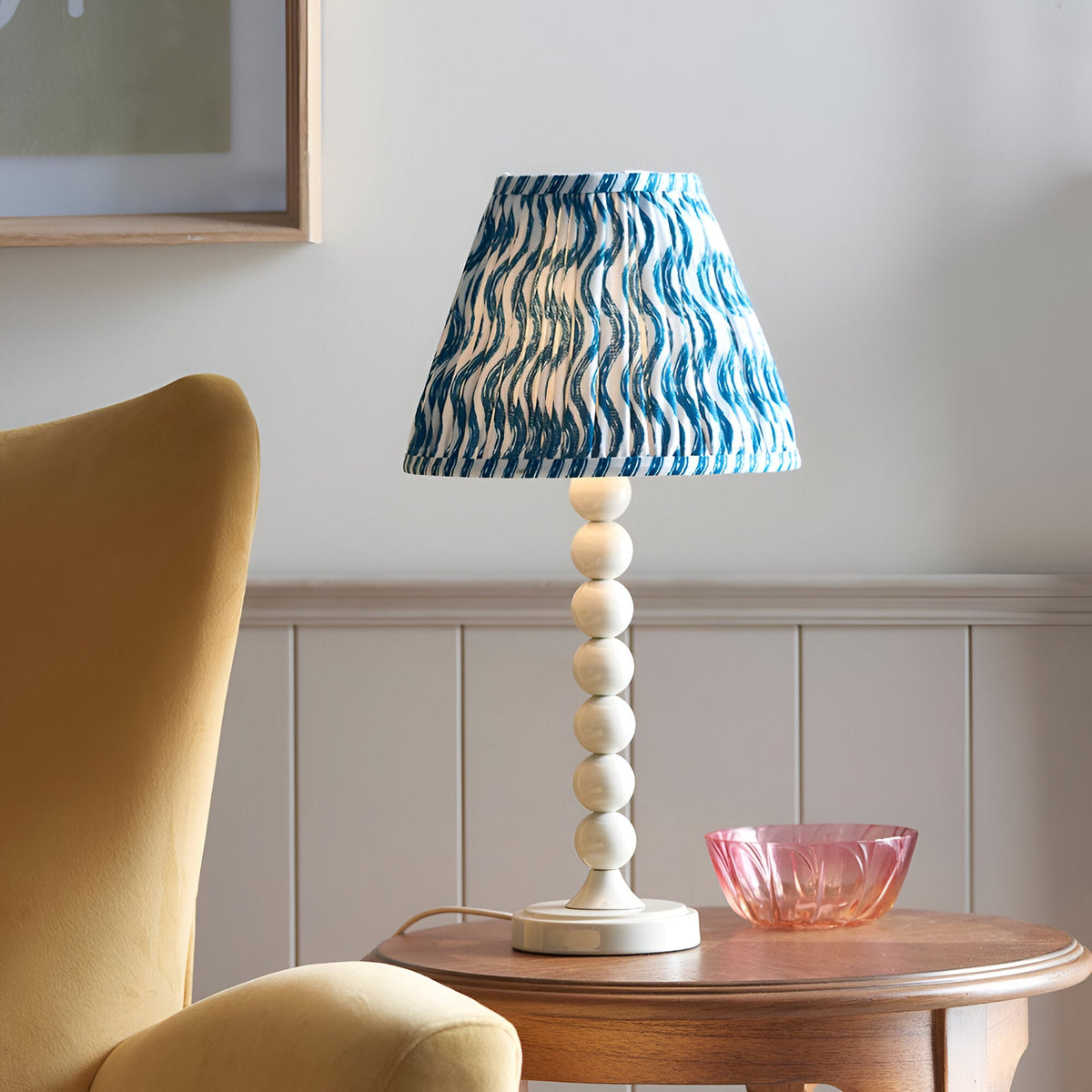 Endon Brenleigh Ripple table lamp with stacked white sphere base and blue and white pleated ripple shade on a wooden side table beside a yellow armchair.