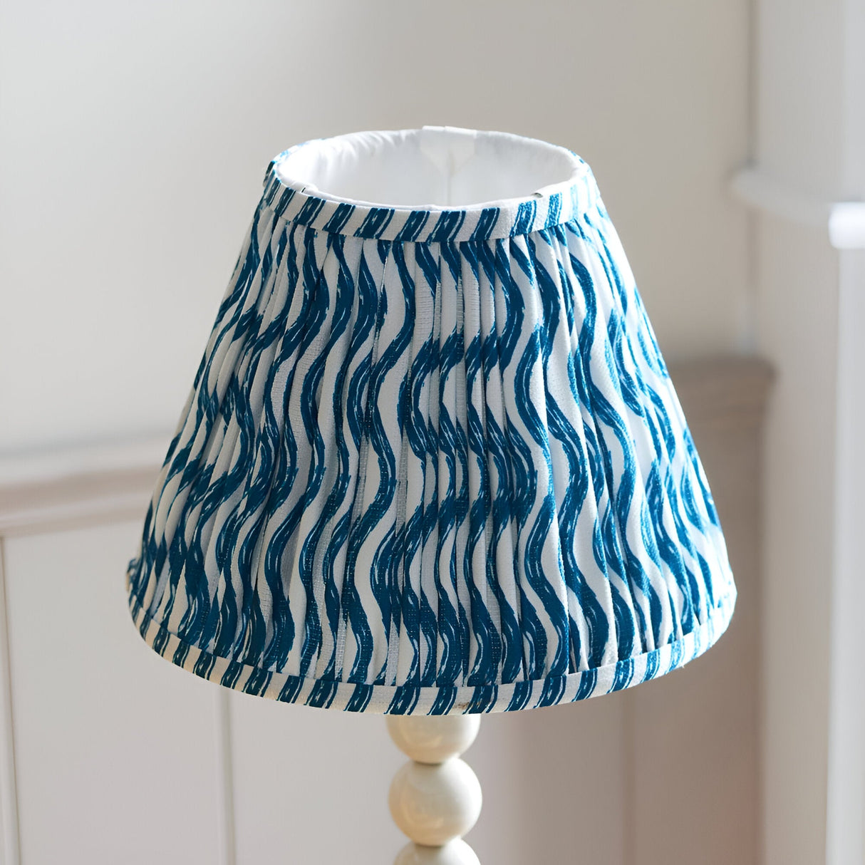 Endon Brenleigh Ripple table lamp with a pleated white and blue wavy-print fabric shade on a gloss white stacked-sphere base.