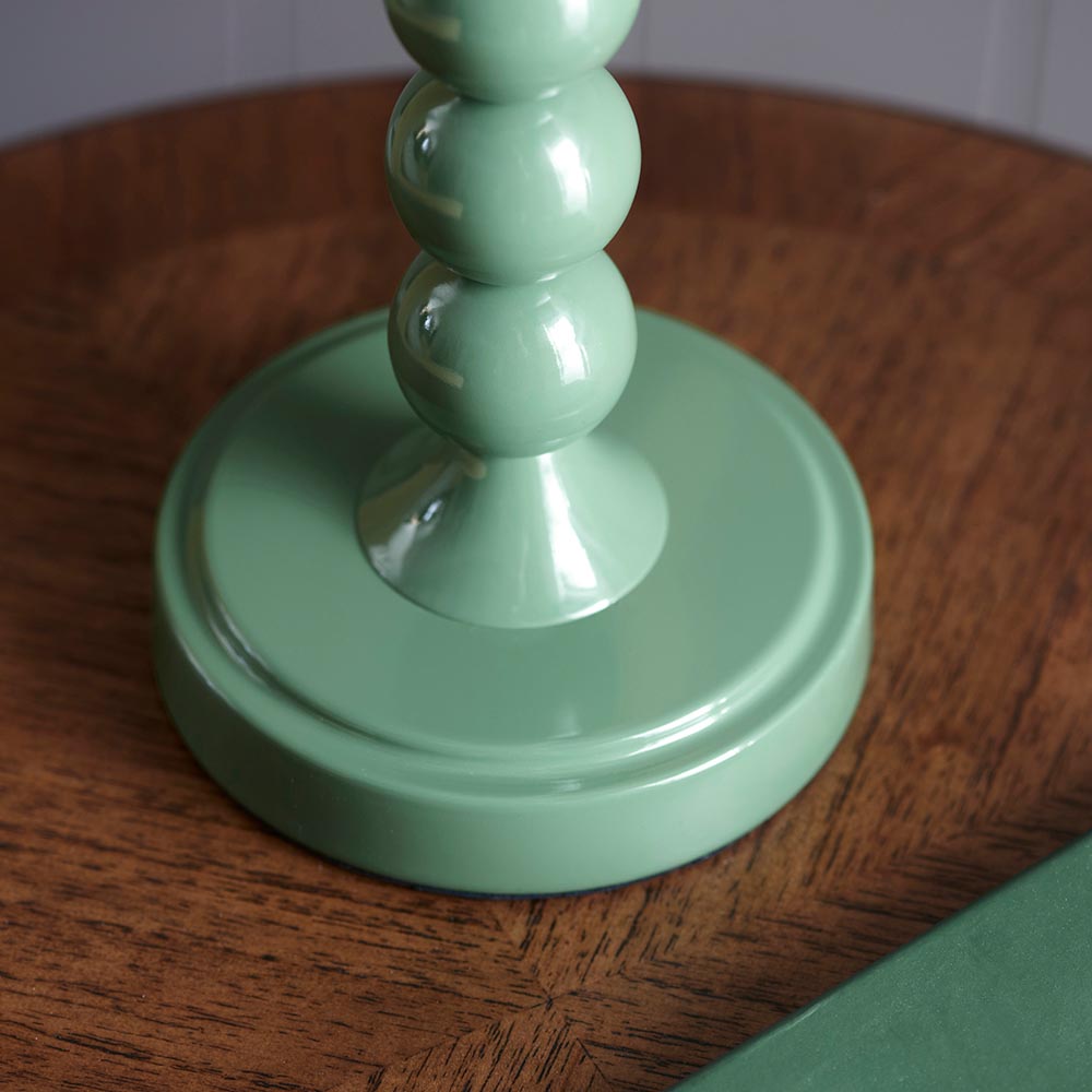 Close-up of the Brenleigh Ikat table lamp's stacked-sphere metal base in glossy green, shown on a wooden table.