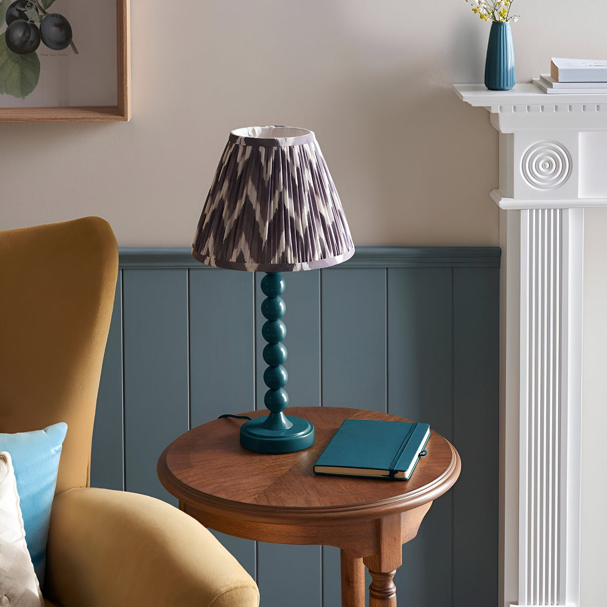 Endon Brenleigh Zigzag table lamp with stacked-sphere teal metal base and grey zigzag pleated shade on a wooden side table in a living room.