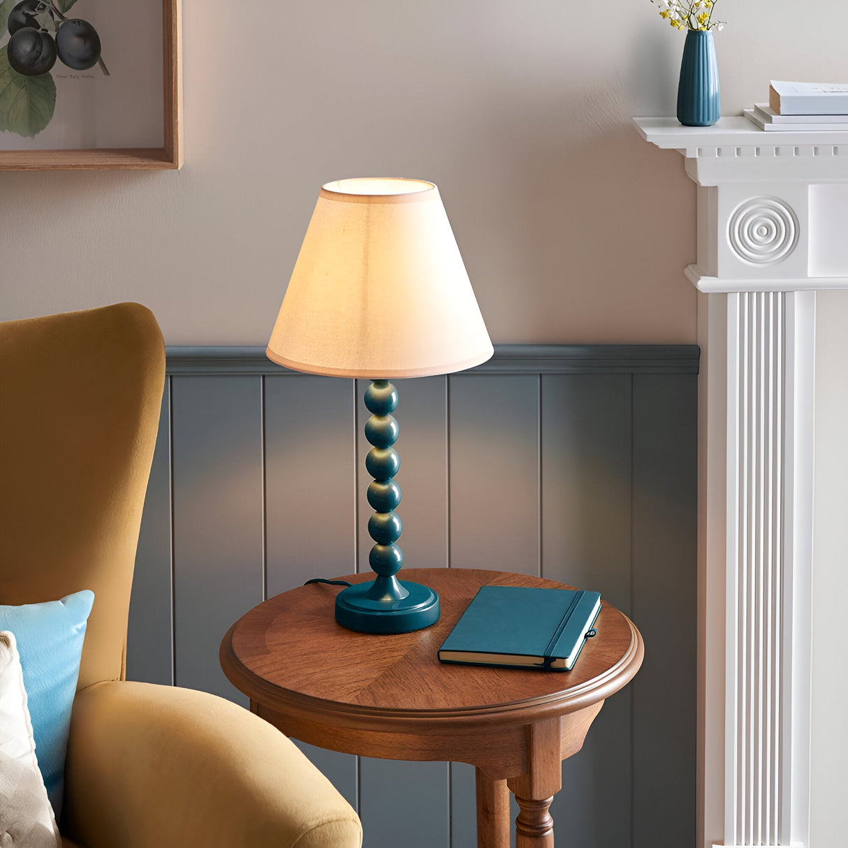 Brenleigh Ivy Table Lamp with blue stacked-sphere metal base and white fabric shade, styled on a wooden side table in a living room.