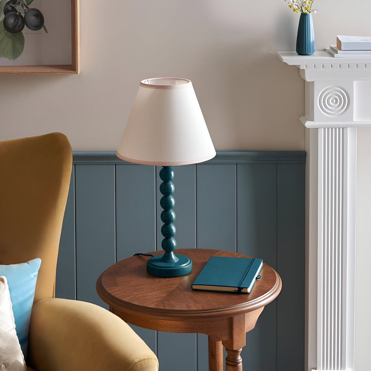 Brenleigh Ivy Table Lamp with blue stacked-sphere metal base and white cotton-mix Ivy shade, styled on a wooden side table in a living room.