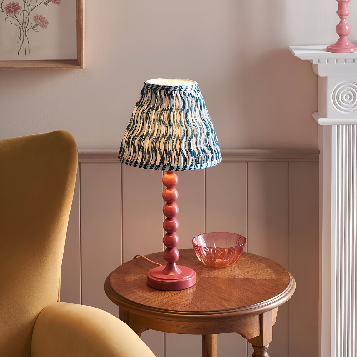 Endon Brenleigh Ripple table lamp with pink stacked-sphere base and blue rippled pleated shade on a wooden side table beside a yellow armchair.