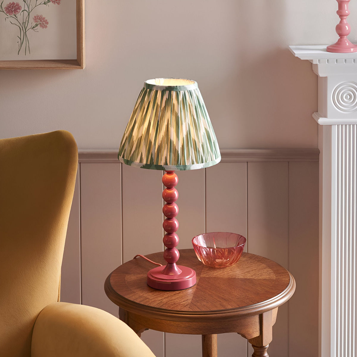 Endon Brenleigh Zigzag table lamp with pink stacked-sphere base and green pleated zigzag shade on a wooden side table beside a mustard armchair.