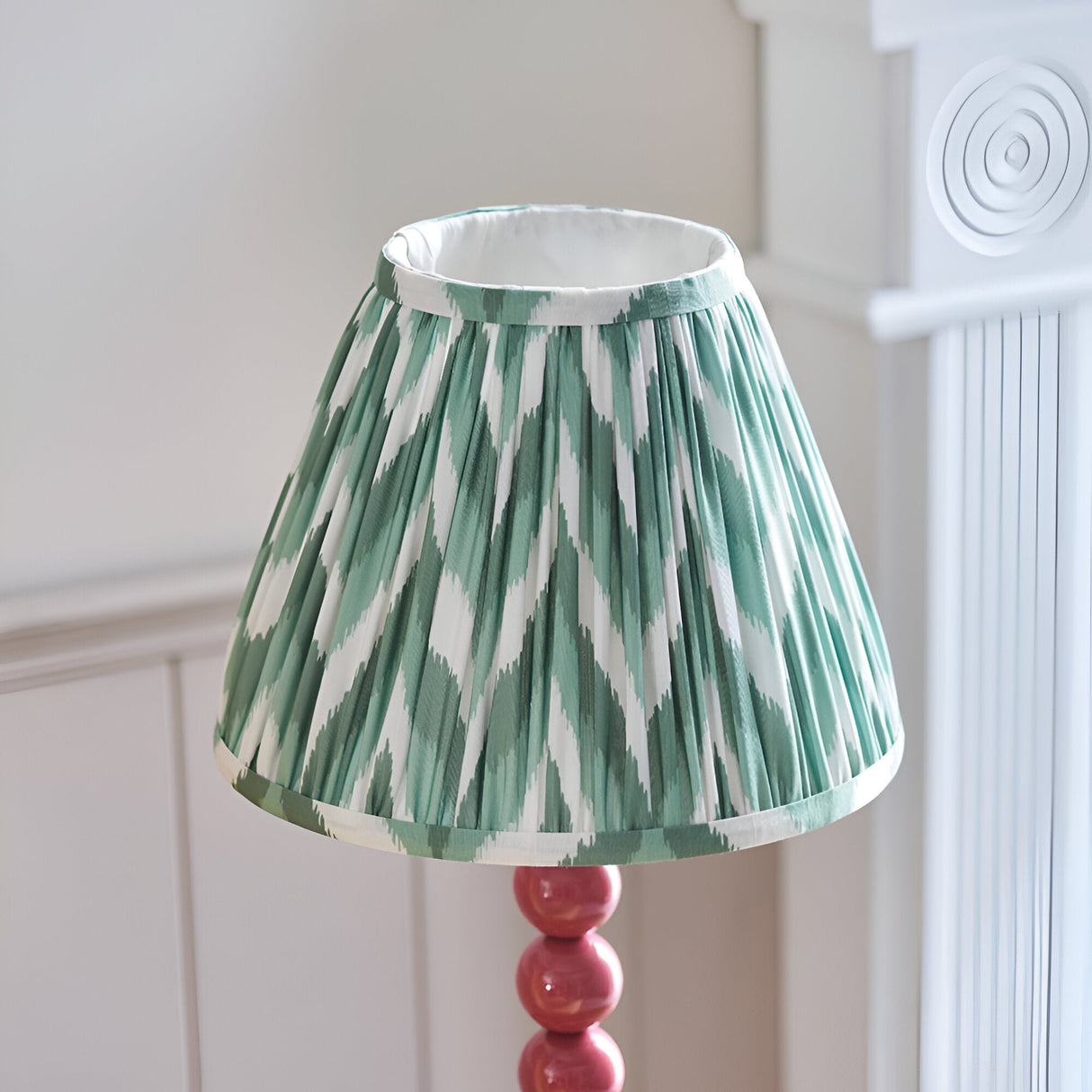 Endon Brenleigh Zigzag table lamp with a pleated green and white chevron faux silk shade on a glossy pink stacked-sphere base, beside white panelling.