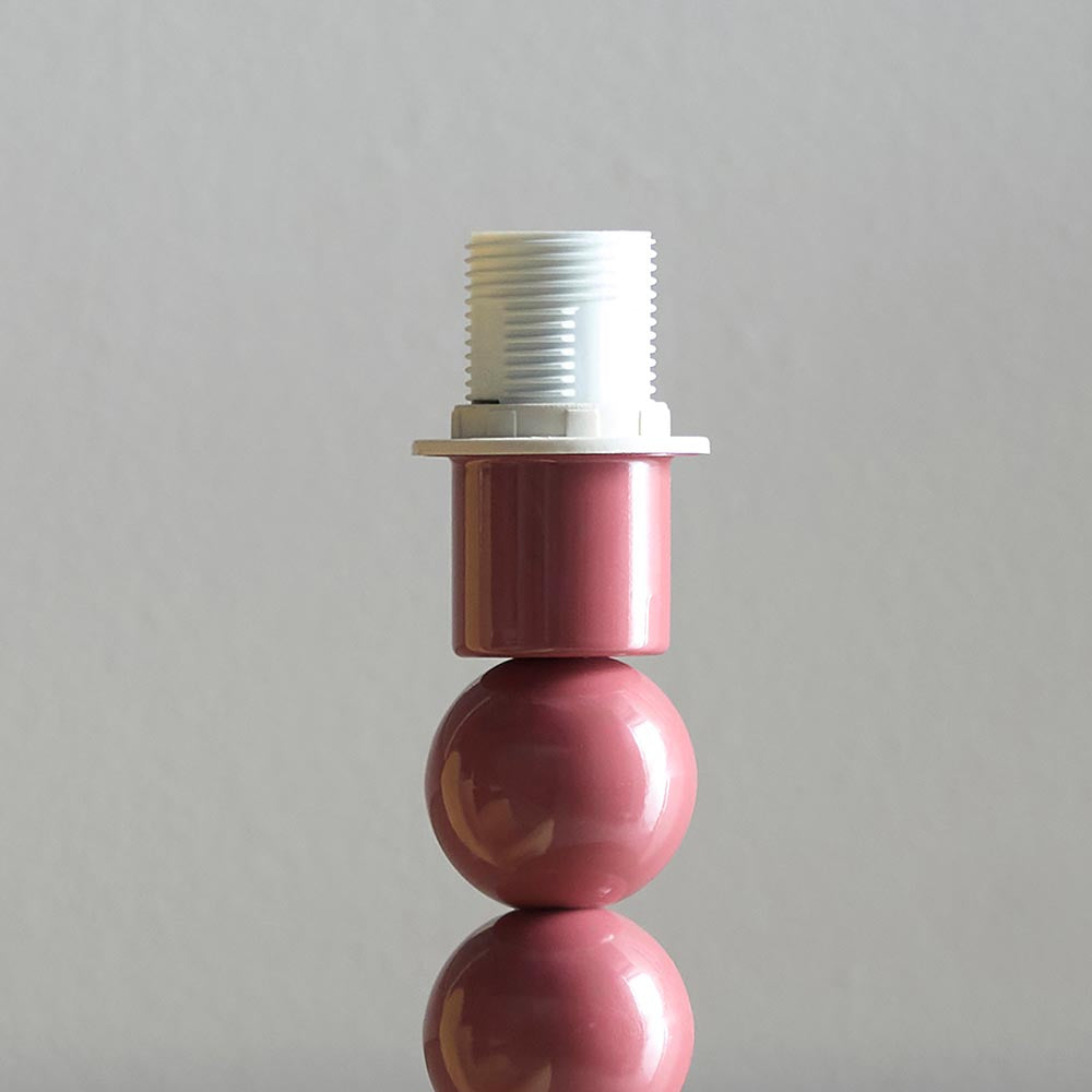 Close-up of the Brenleigh Zigzag Table Lamp's pink gloss stacked-sphere metal base with white threaded E14 bulb fitting, shown against a plain grey background.