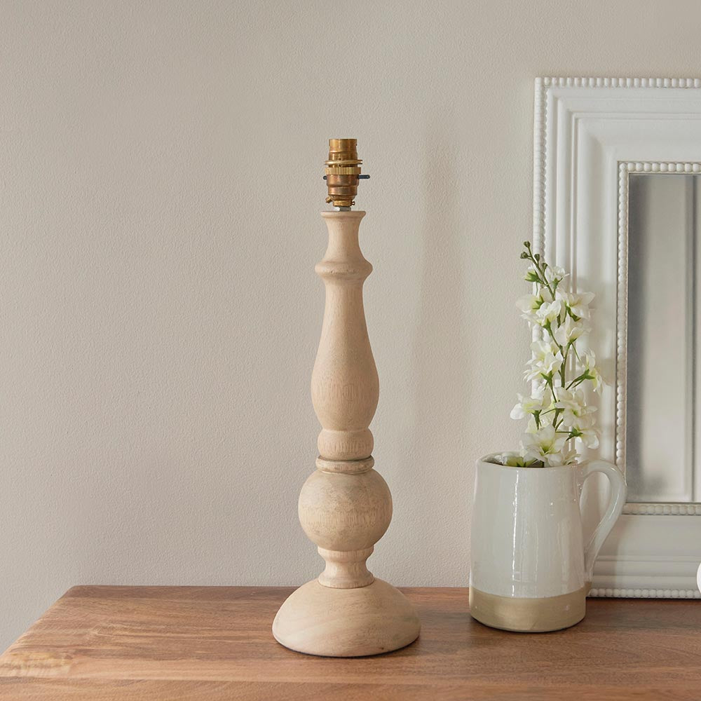 Endon Brenhurst table lamp base in hand-turned natural wood with brass B22 lamp holder, styled on a wooden sideboard beside a white jug and mirror.
