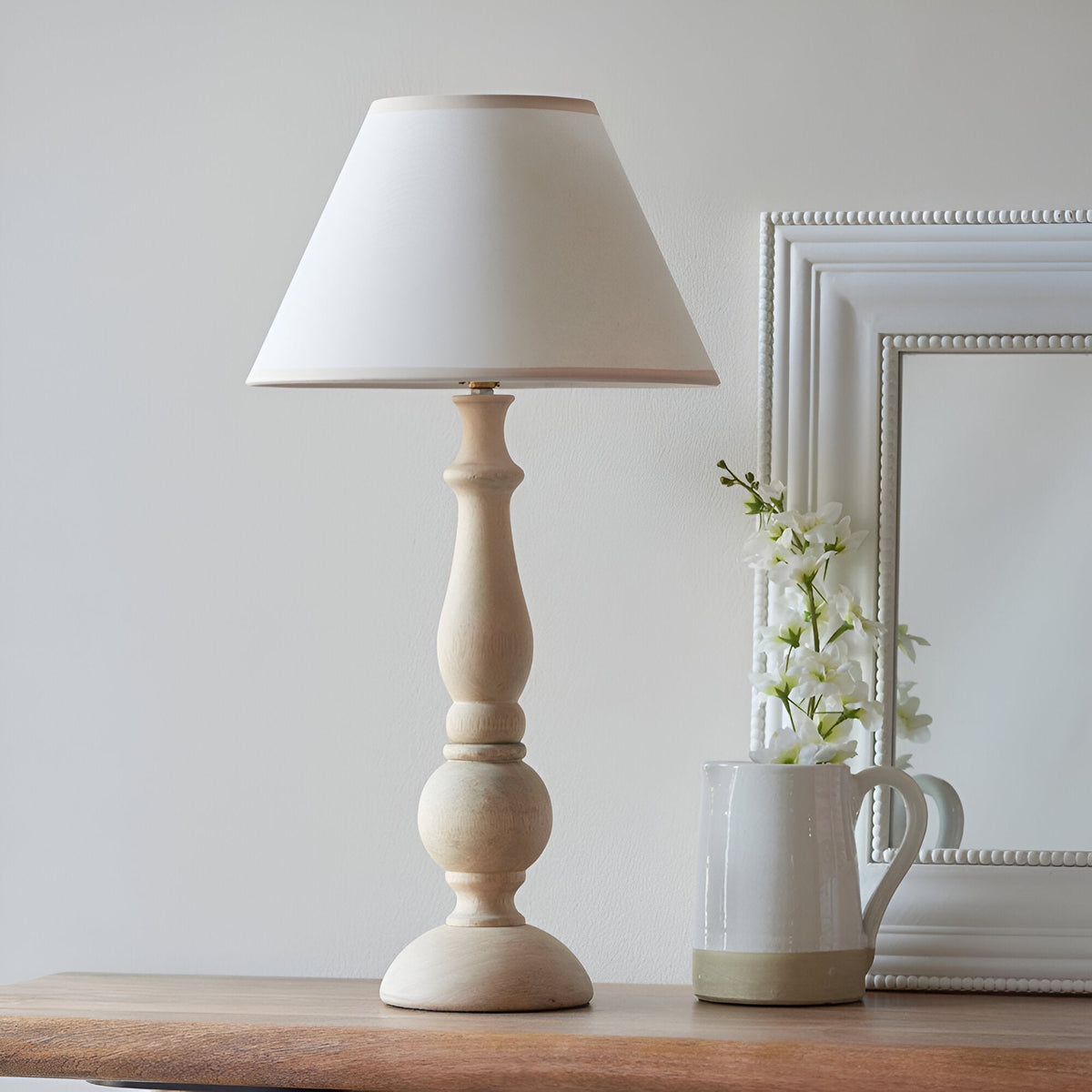 Brenhurst Table Lamp in Vintage White, hand-turned wood base with tapered cotton-mix shade, styled on a wooden surface beside a jug and flowers.