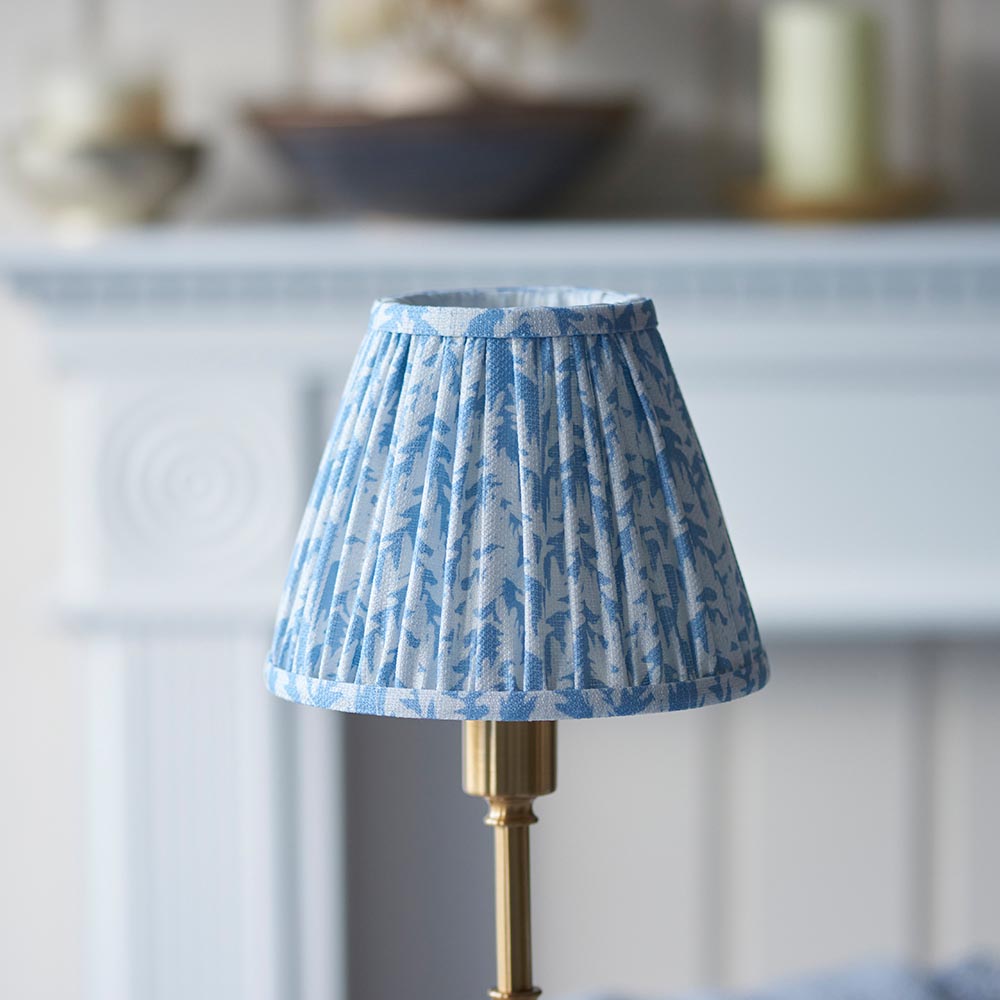 Ashstead LED Leaf Table Lamp with pleated blue and white leaf-print fabric shade on a brass base, shown on a mantelpiece setting.