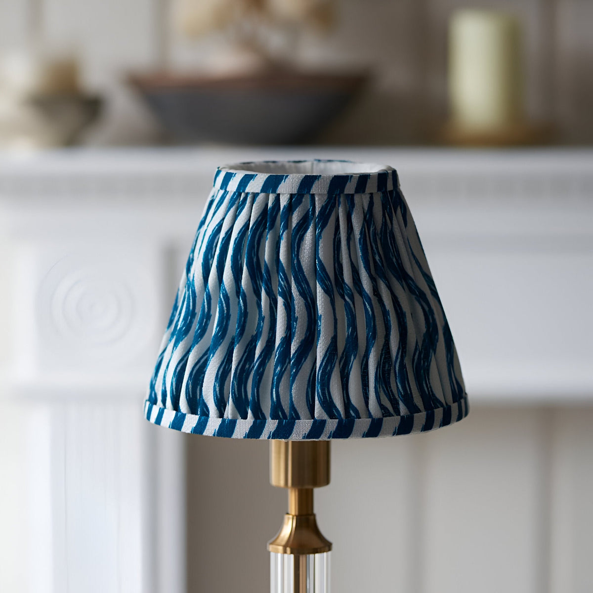 Endon Carlwood LED table lamp with brushed brass base and pleated marlin blue Ripple shade in a wavy print, shown on a mantel setting.
