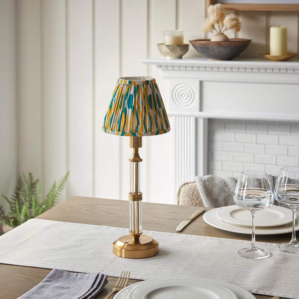 Carlwood LED table lamp with brass base, ribbed glass column, and yellow-green Ikat print shade, styled on a dining table near a white mantel.