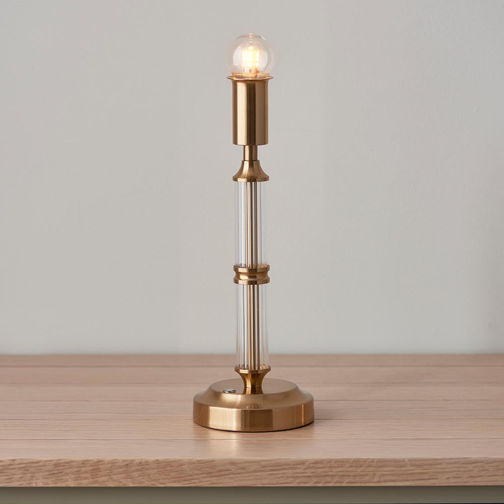 Carlwood LED table lamp with slim brass column, ribbed glass rods, and exposed globe bulb, shown lit on a light wood surface against a plain background.