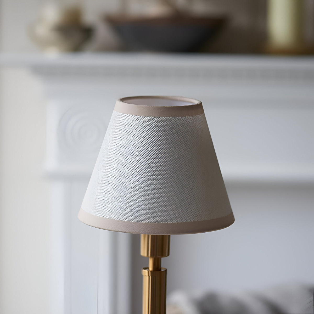 Danebourne LED Rechargeable Table Lamp with tapered fabric shade in white and brass, on a stepped brass base, set against a blurred neutral interior.