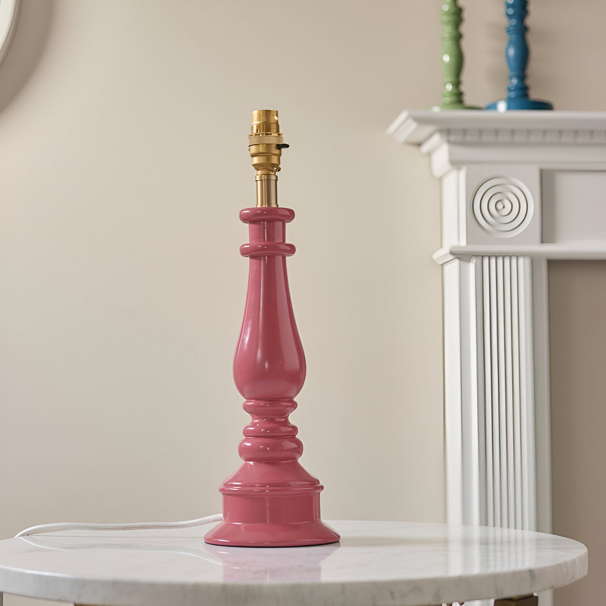 Endon Carlworth table lamp base in glossy pink turned resin with a brass B22 holder, displayed on a marble side table beside a white mantelpiece.