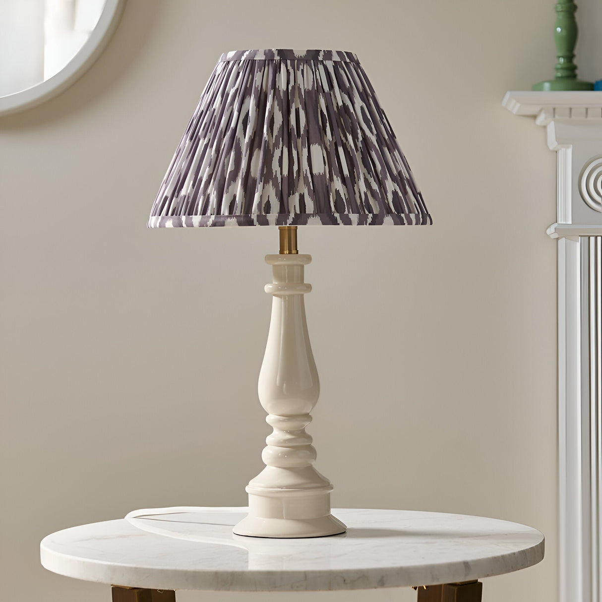 Carlworth Ikat Table Lamp with cream turned resin spindle base and pleated grey patterned fabric shade, shown on a marble side table in a living room.