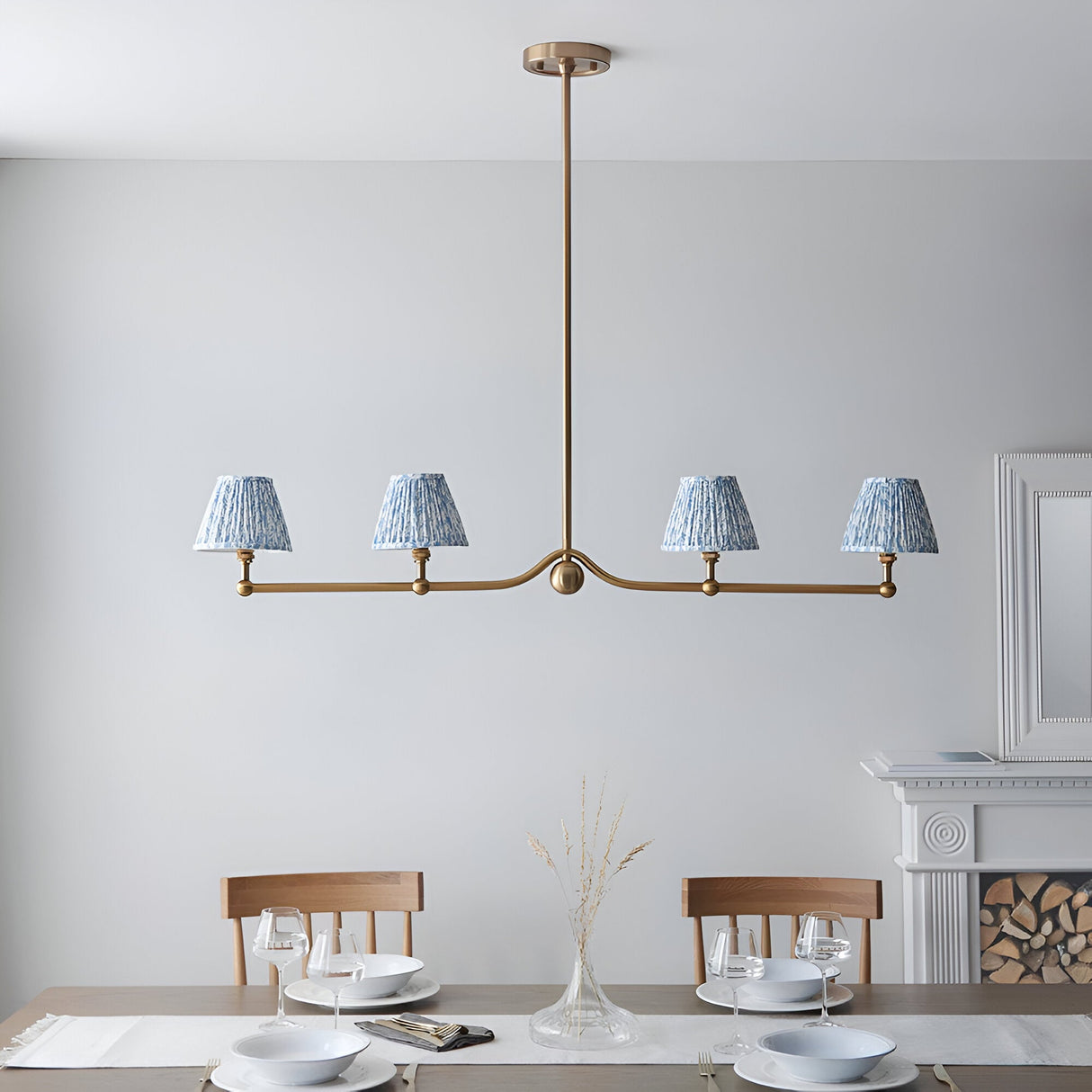 Endon Cliffleigh Leaf 4 light linear pendant in brushed brass with four tapered blue leaf-print shades, above a dining table by a fireplace.