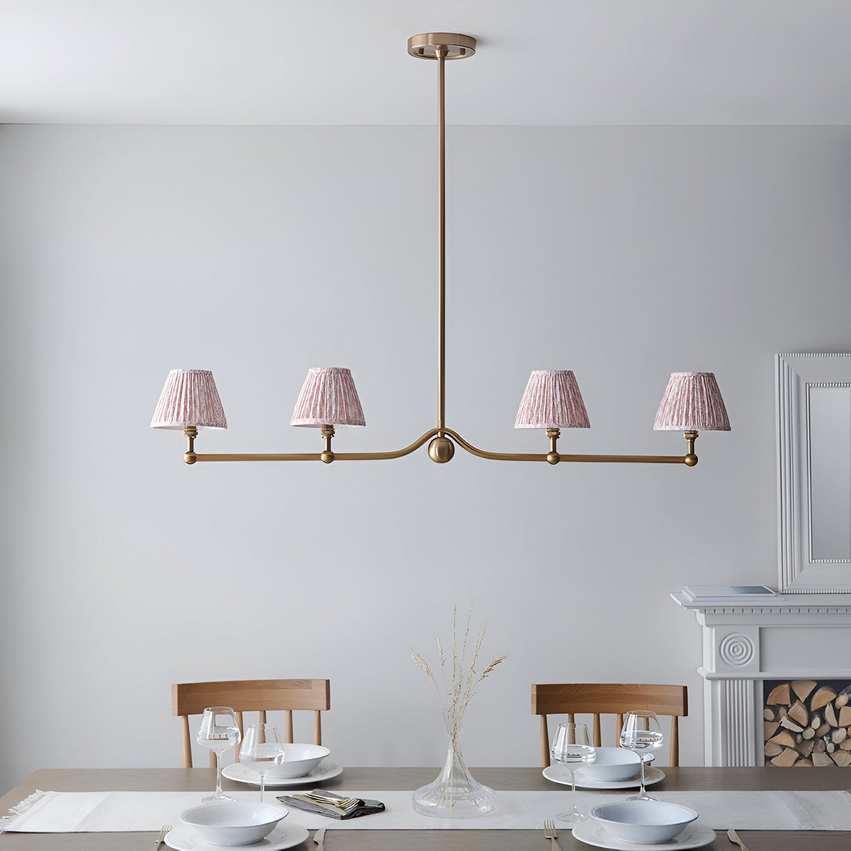 Cliffleigh Leaf 4 Light Linear Pendant in brushed aged brass with pleated pink fabric shades, hung above a dining table in a light-toned room.