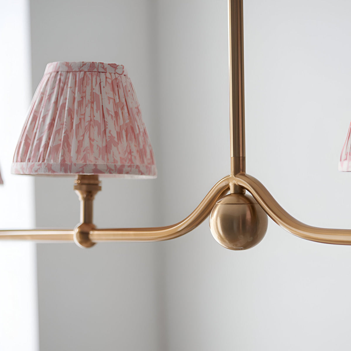Close-up of the Cliffleigh Leaf 4 Light Linear Pendant in brushed brass, showing a pink patterned tapered shade and sphere detail on the curved bar.