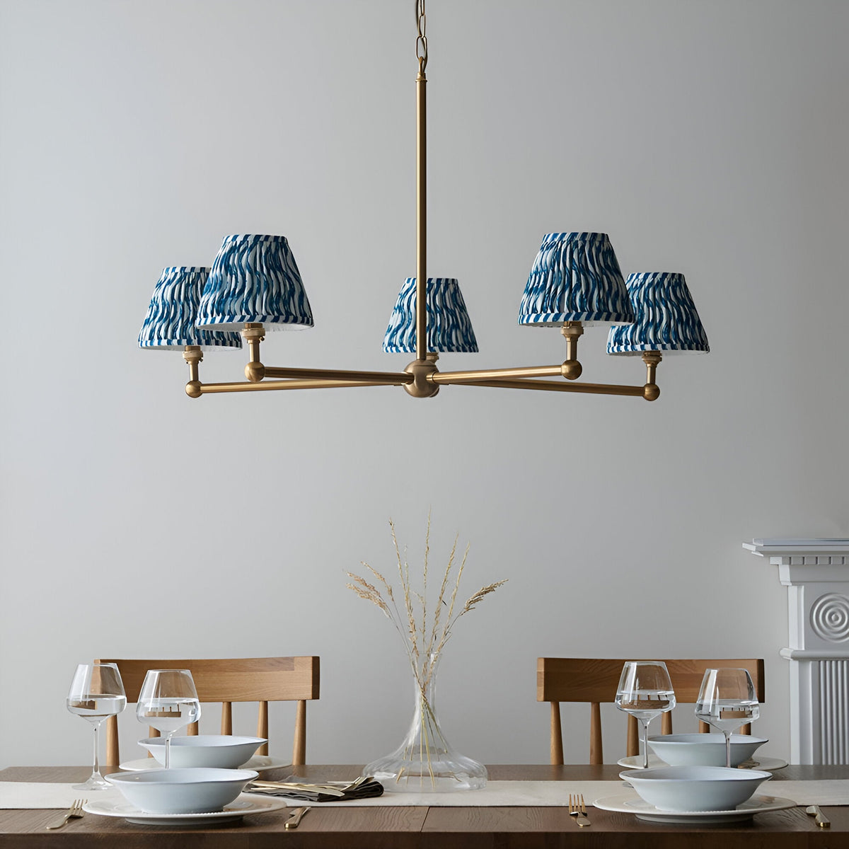 Cliffleigh 5 Light Ripple Pendant in Blue, brushed aged brass frame with five tapered blue patterned fabric shades, shown above a dining table.