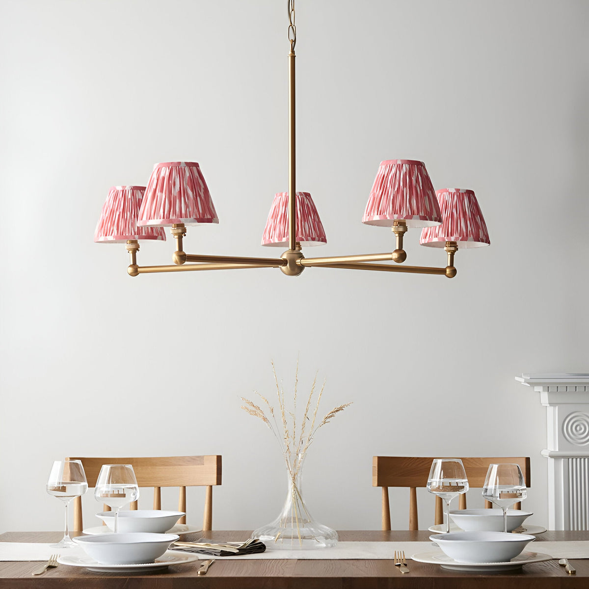 Endon Cliffleigh Ikat 5 light pendant in brushed brass with pink Ikat pleated tapered shades, shown above a wooden dining table set with glassware.