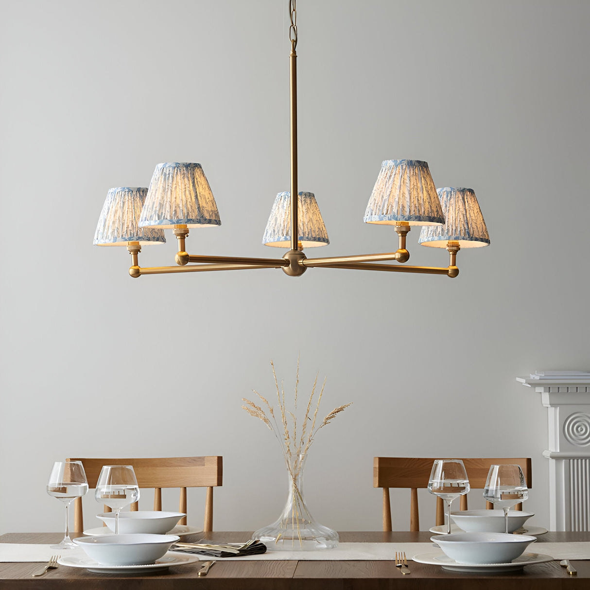 Endon Cliffleigh Leaf 5 light pendant with brushed brass arms and pleated blue leaf-print fabric shades, above a wooden dining table setting.