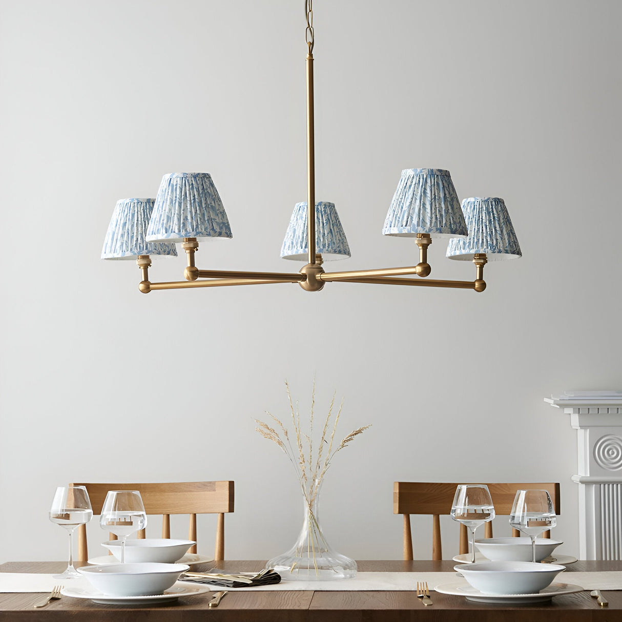 Endon Cliffleigh Leaf 5 light pendant with brushed brass frame and tapered pleated blue leaf-print shades, above a dining table setting.