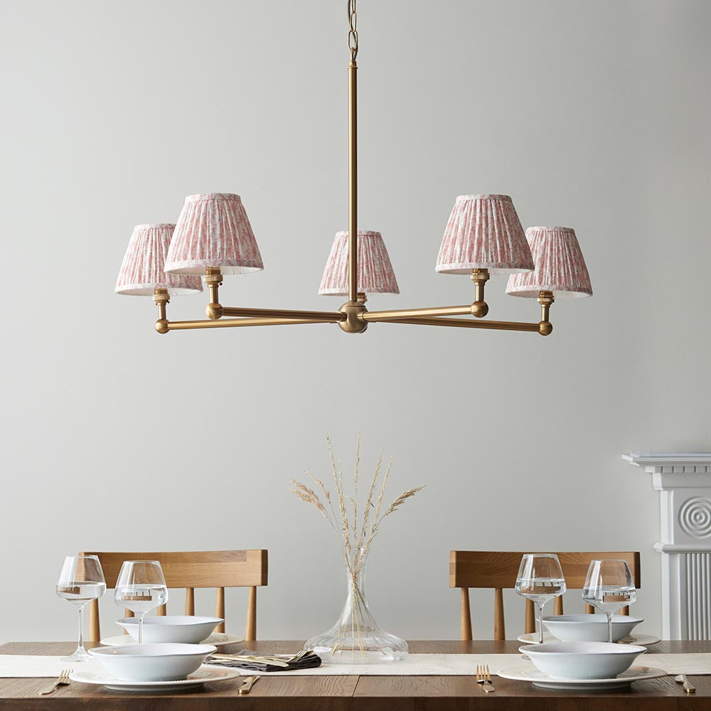 Cliffleigh Leaf 5 Light Pendant in brushed brass with five pleated pink Leaf-pattern shades, shown above a wooden dining table set with tableware.