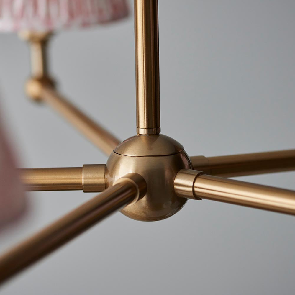 Close-up of the Cliffleigh Leaf 5 Light Pendant's brushed brass hub and arms, showing pink patterned shade edges against a plain grey background.
