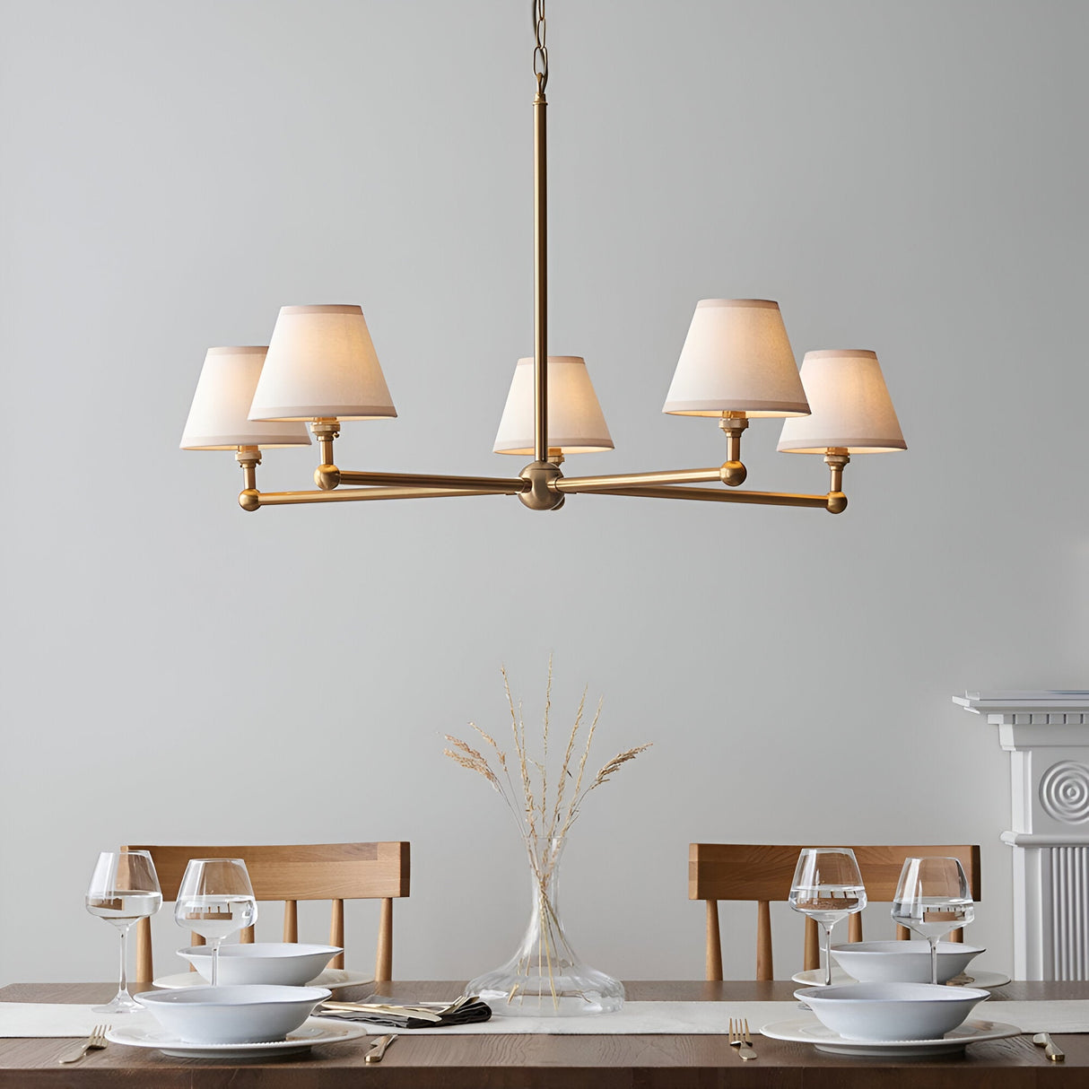 Endon Cliffleigh 5 light pendant in brushed aged brass with white tapered fabric shades, hung above a wooden dining table set with glassware.