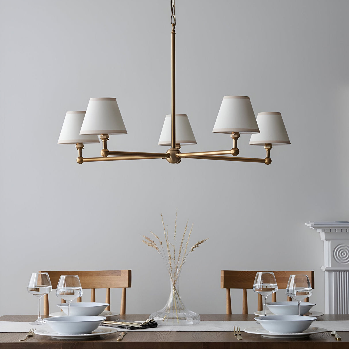 Endon Cliffleigh 5 light pendant in brushed aged brass with white tapered fabric shades, hung above a wooden dining table set for two.