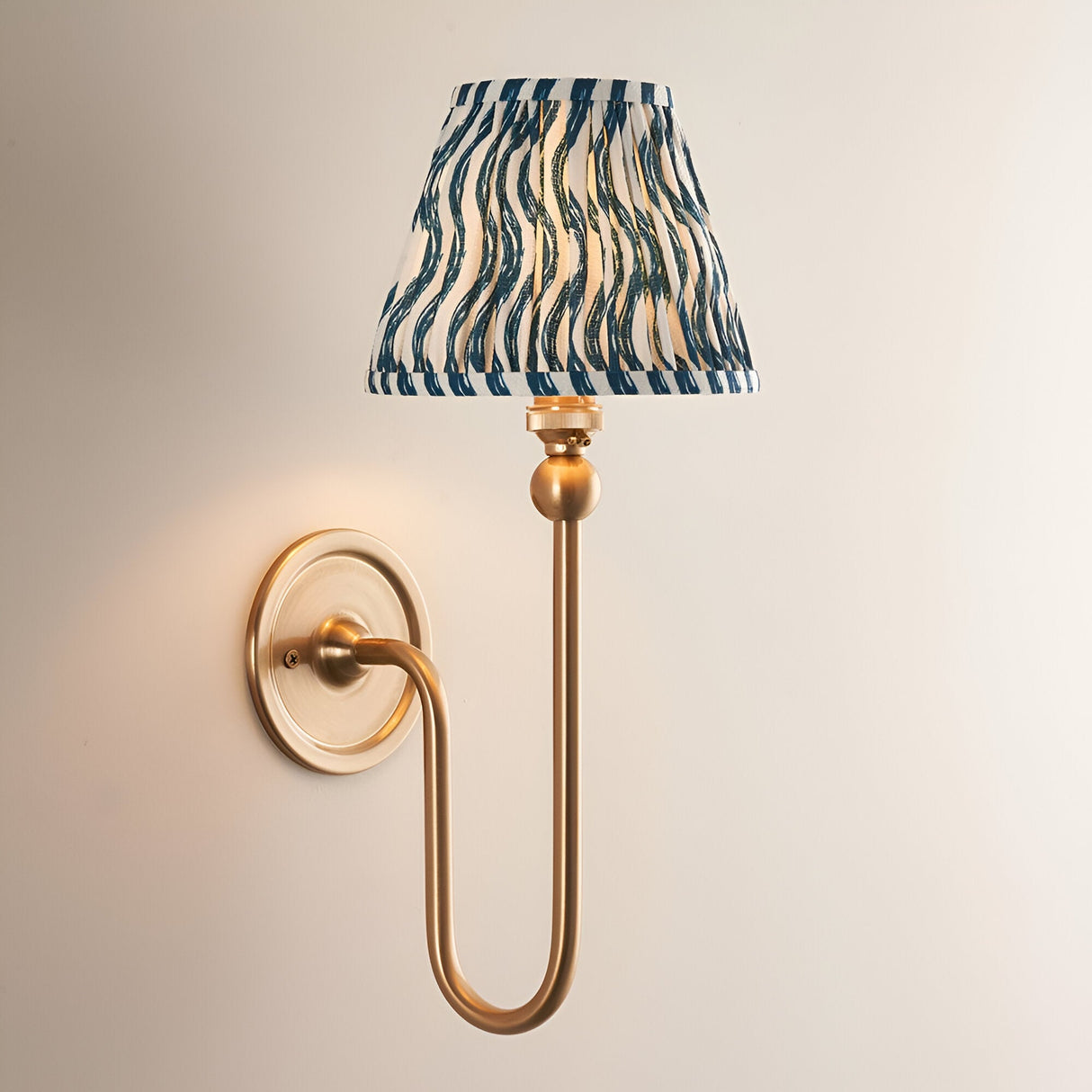 Endon Cliffleigh wall light in brushed aged brass with a tall curved arm and pleated marlin blue faux linen shade in a ripple design.