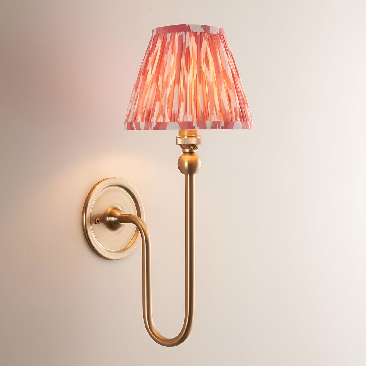 Endon Cliffleigh Ikat wall light in brushed brass with a curved arm and tapered pleated shade in coral pink ikat-printed faux silk.