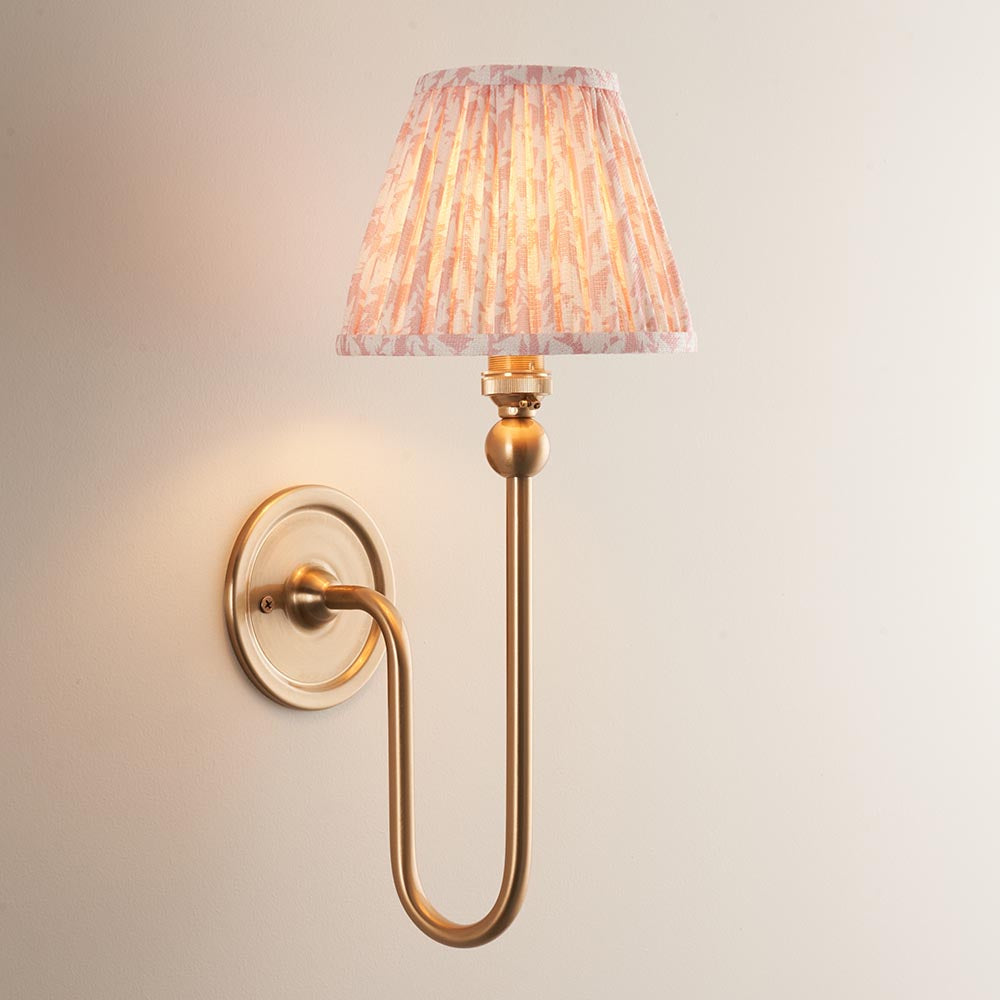 Endon Cliffleigh Leaf Wall Light II in brass, a curved single-arm wall light with a pleated peach leaf-print tapered fabric shade on a neutral wall.