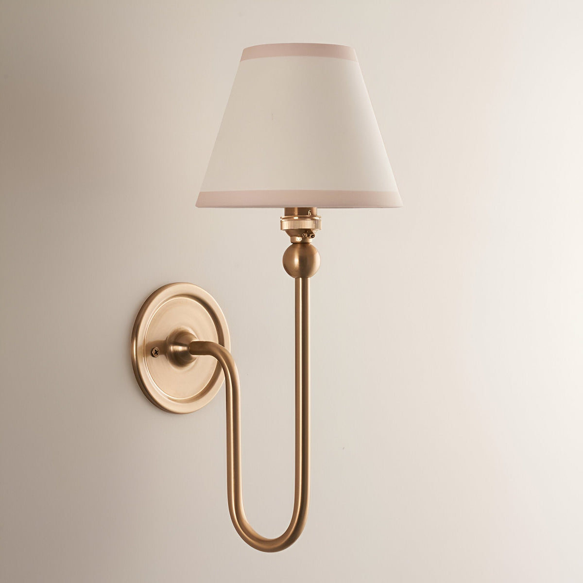 Cliffleigh Ivy wall light in brushed aged brass with a tapered ivory fabric shade and almond edge trim, shown on a plain light background.
