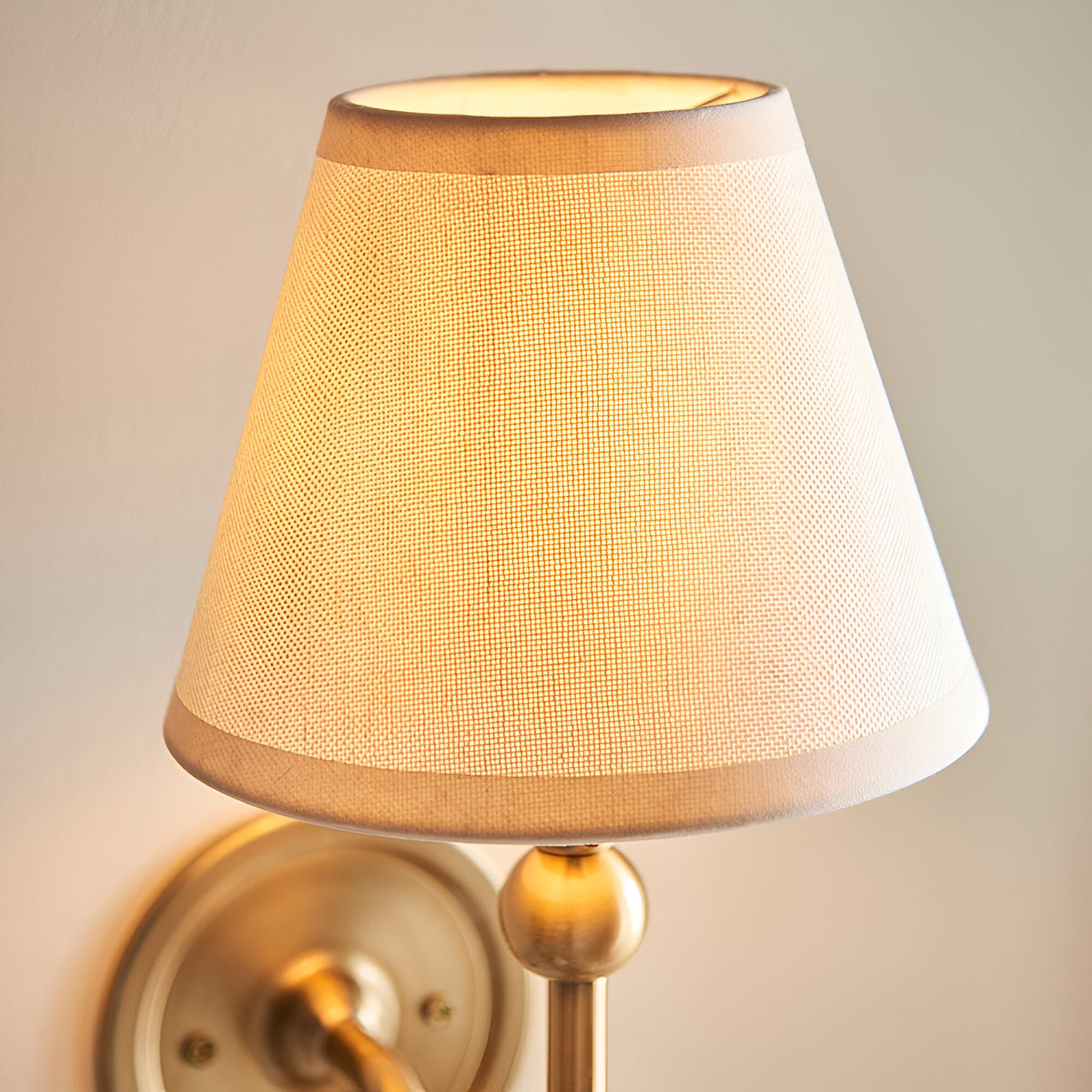 Cliffleigh Ivy Wall Light in vintage white, tapered fabric shade with taped edge on a brushed aged brass backplate, close-up view.