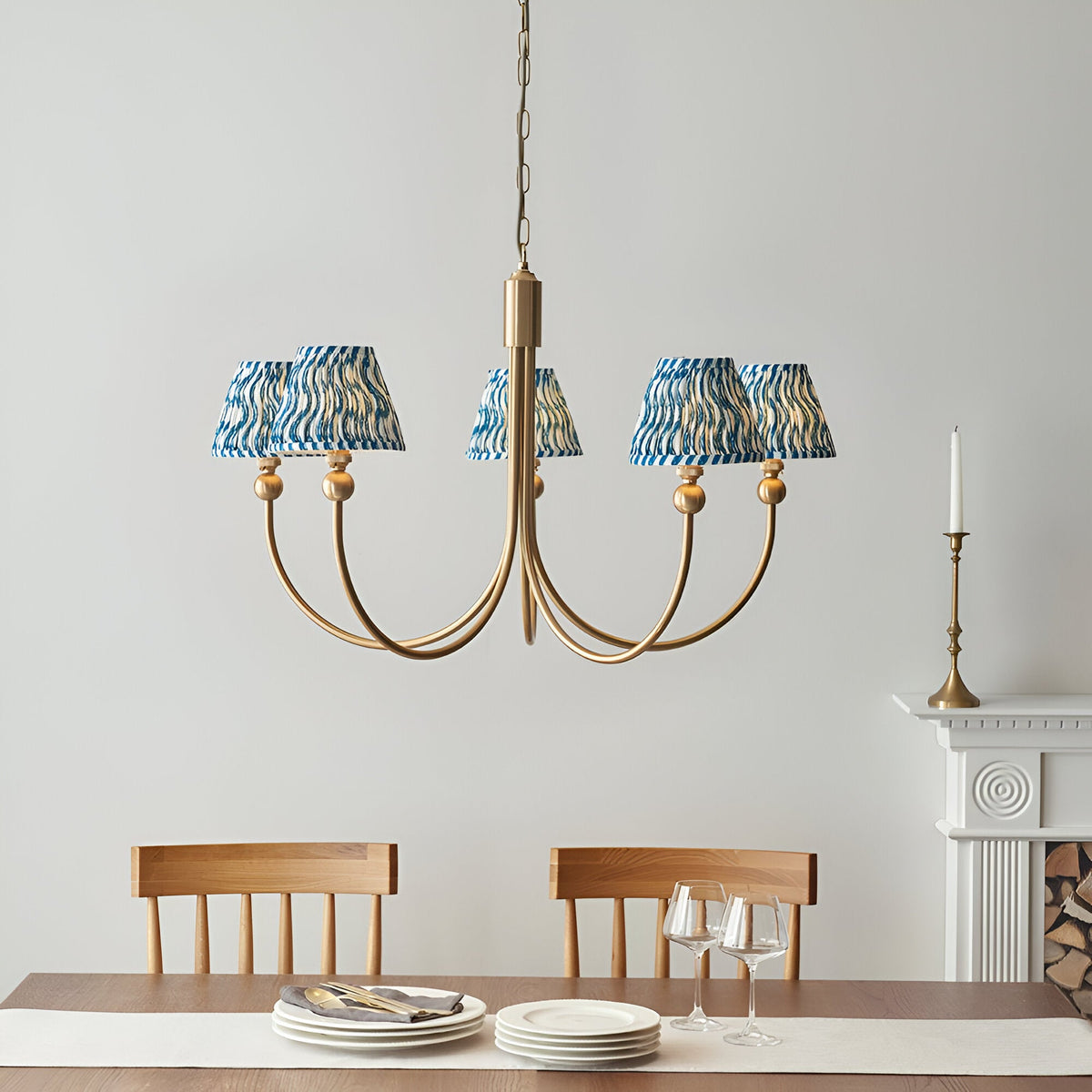 Endon Cliffleigh 5 light curved-arm pendant in brushed aged brass with marlin blue rippled fabric shades, hung above a dining table by a fireplace.
