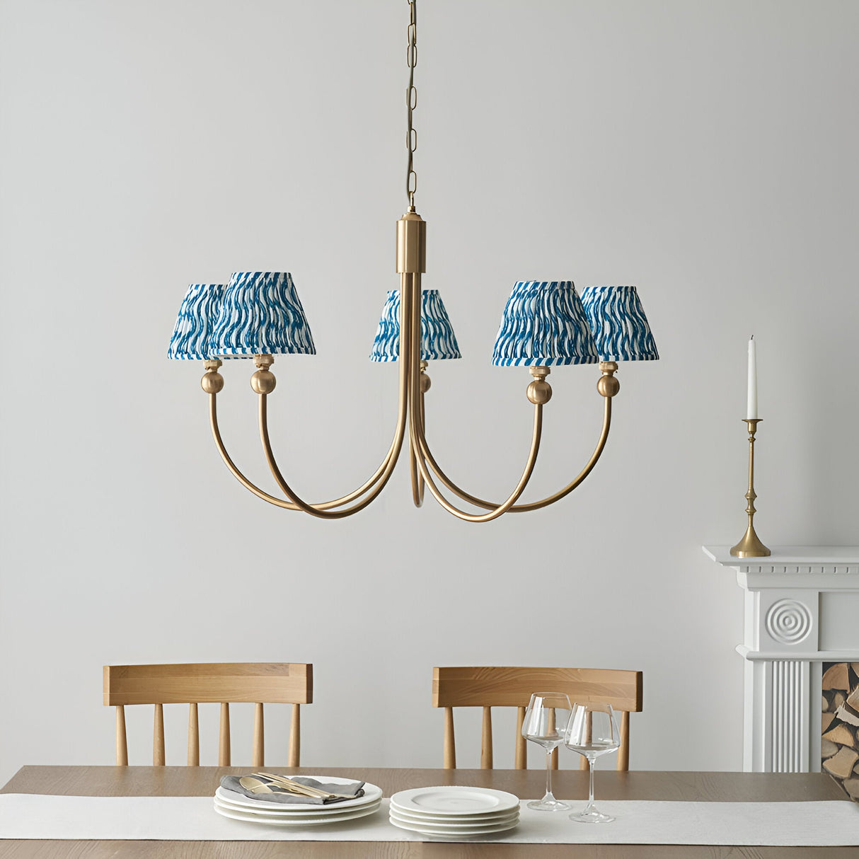 Endon Cliffleigh 5 light pendant with curved brushed brass arms and tapered marlin blue ripple fabric shades, hung over a dining table by a fireplace.