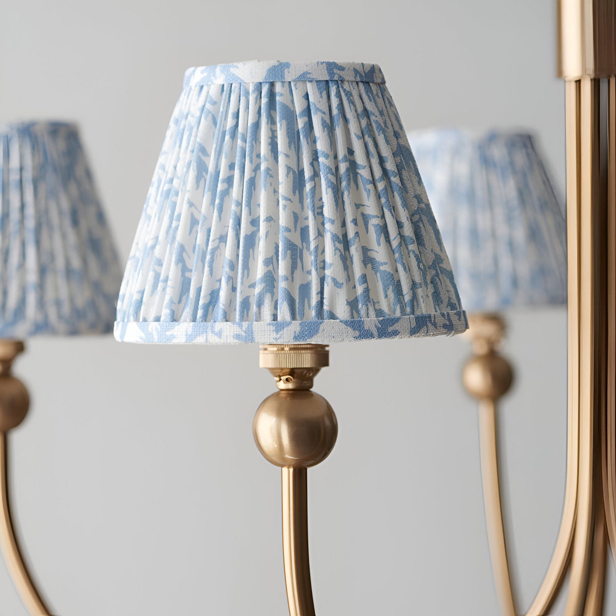 Close-up of Endon Cliffleigh Leaf pendant showing a tapered pleated shade in blue leaf print on faux linen, mounted on a brushed aged brass curved arm.