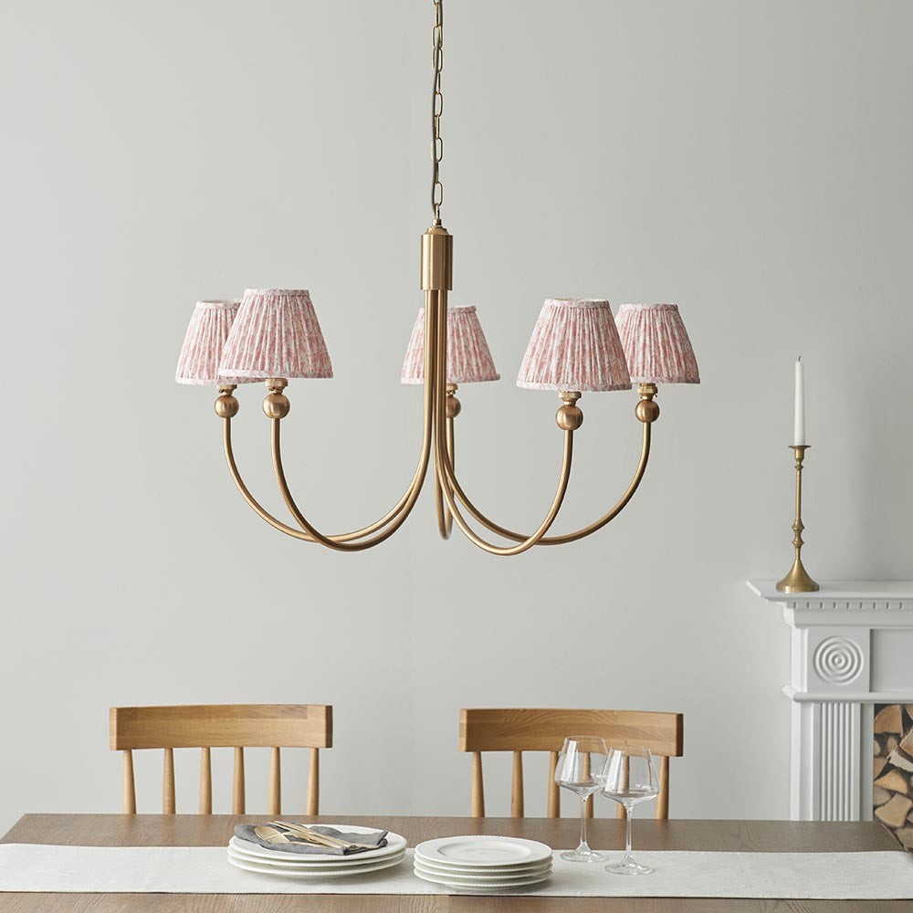 Cliffleigh Leaf 5 light curved arm pendant in brushed brass with pleated pink patterned shades, hung above a dining table in a light-toned room.