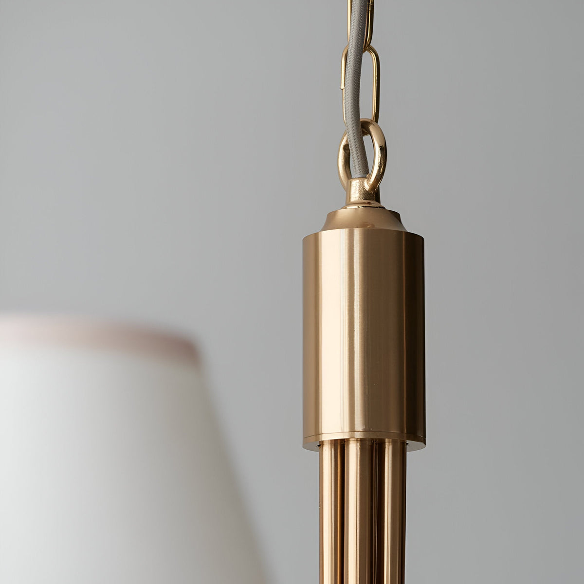 Close-up of the Cliffleigh pendant light's brushed brass ceiling hook and chain, with a tapered white fabric shade edge visible against a grey background.