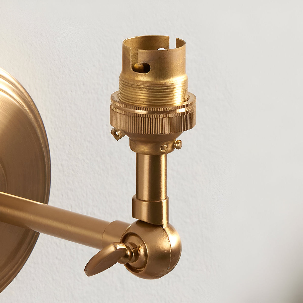 Close-up of the Endon Corven wall light showing its brushed aged brass B22 lampholder, adjustable knuckle arm, and stepped circular backplate.