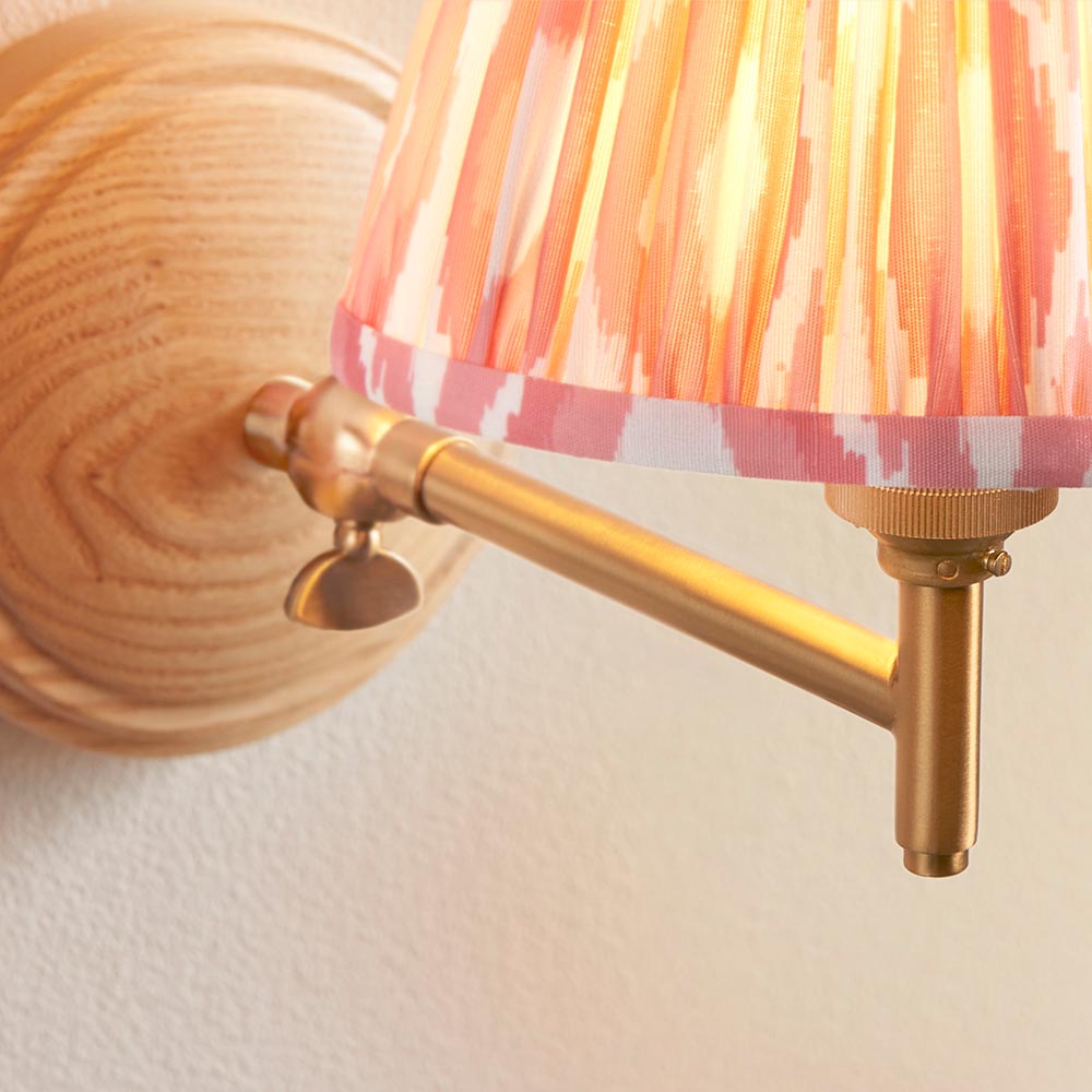 Close-up of the Endon Daneley wall light showing its natural ash wood back, brushed aged brass adjustable knuckle, and linear arm against a white wall.