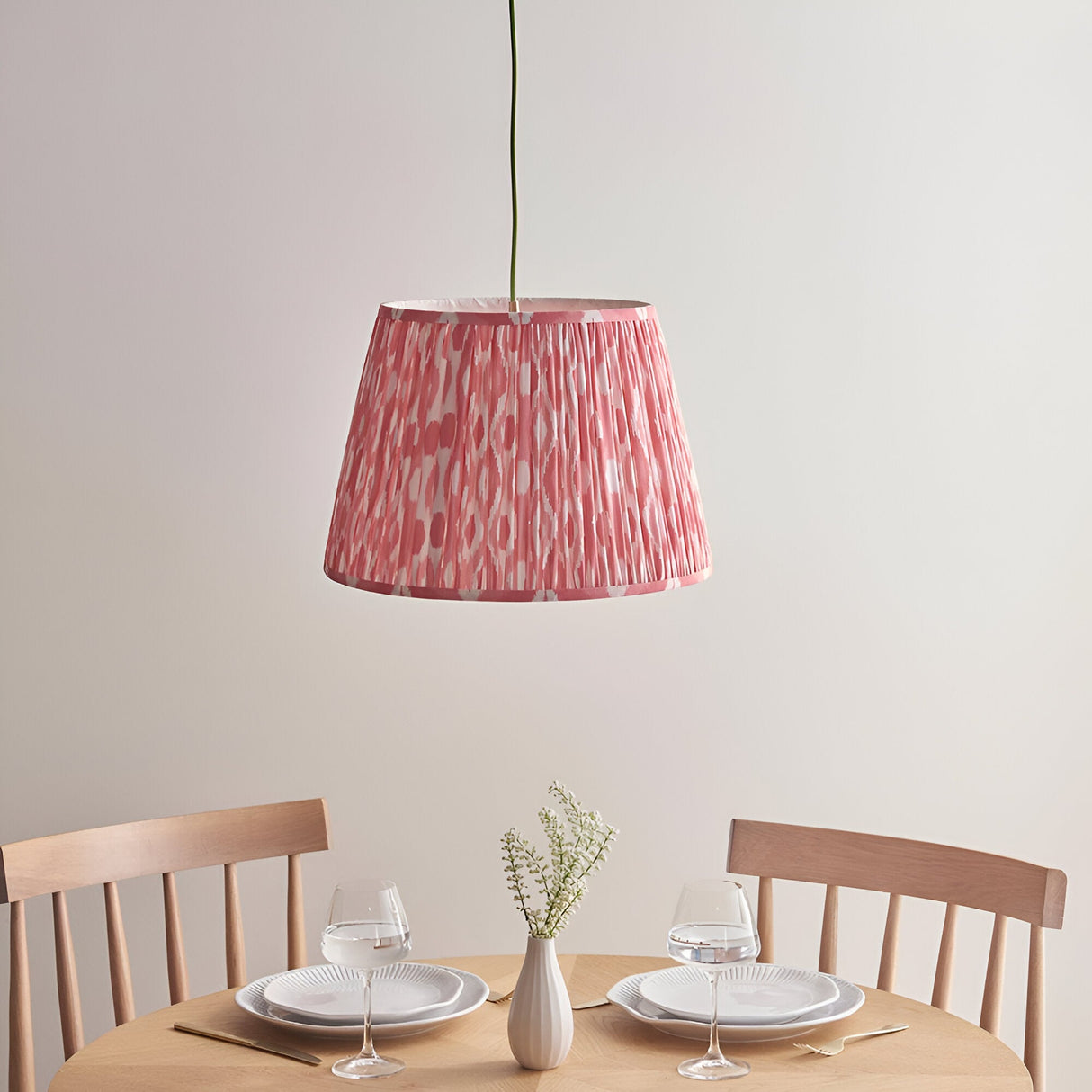 Endon Brackmont Ikat Coral pendant light with handmade pleated faux silk tapered shade and green braided cable, hung above a wooden dining table.