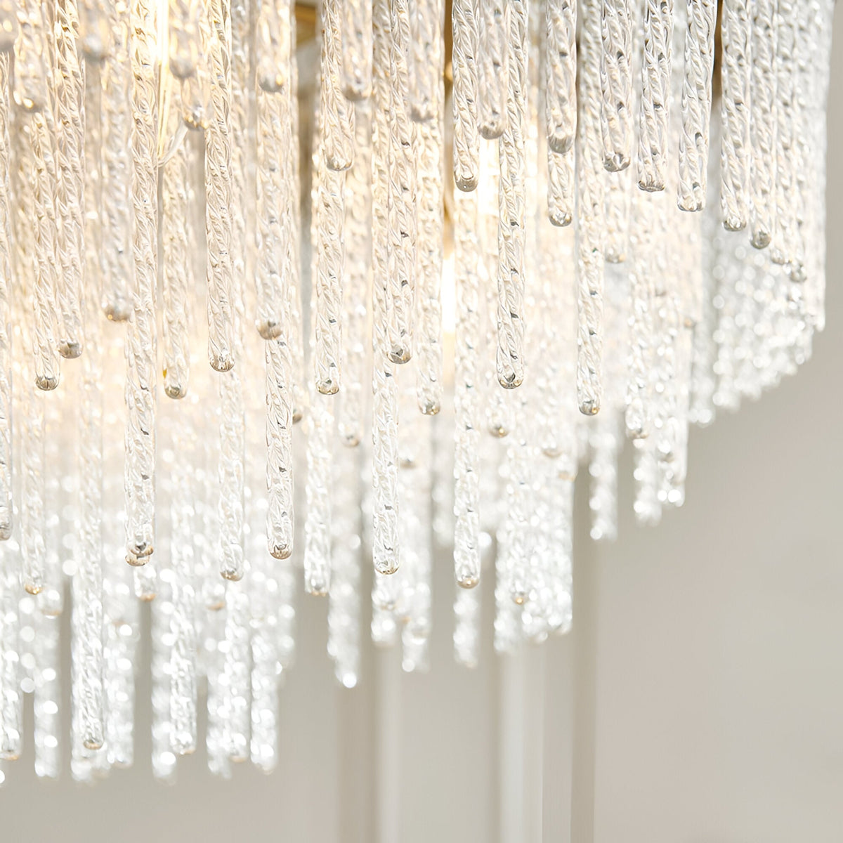 Aldfield nine-light pendant, close-up of twisted clear glass rods cascading from a brushed antique brass frame, lit against a plain light background.