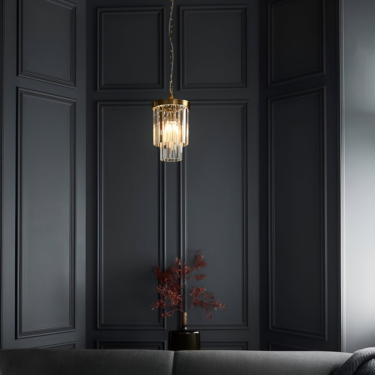 Endon Bevstead small single pendant with tiered clear glass lozenge drops on a brushed aged brass frame, hung in a dark panelled corner.