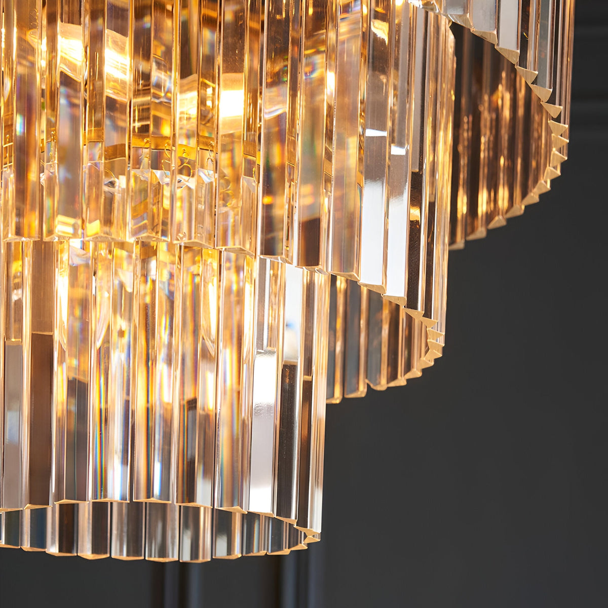 Close-up of Endon Bevstead 7 light pendant showing tiered clear cut lozenge glass drops and brushed brass band against a dark background.