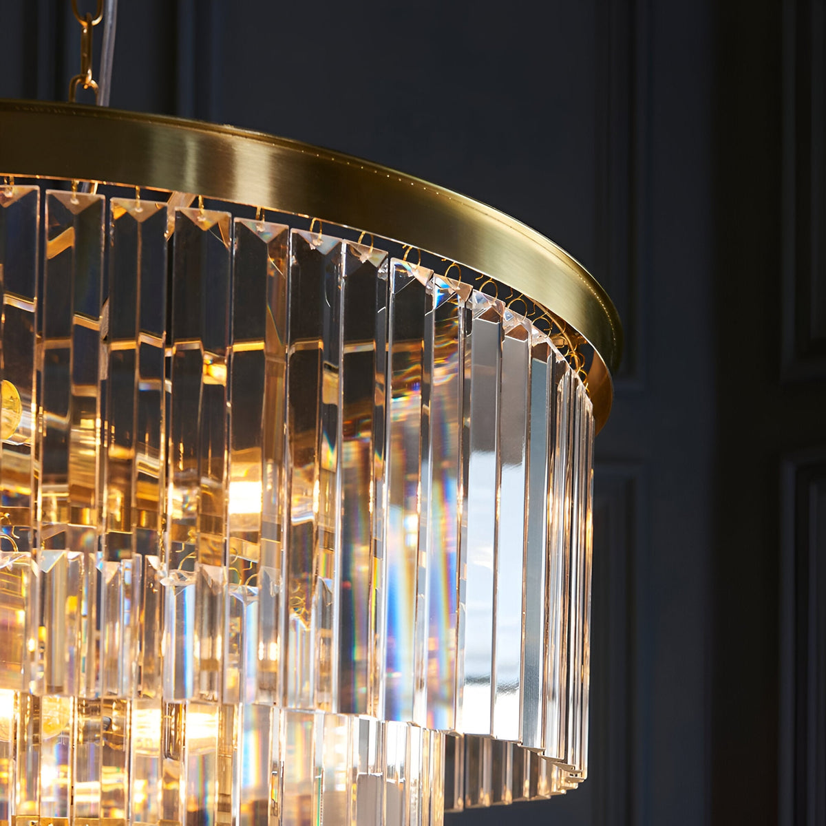 Close-up of the Endon Bevstead 7 light pendant showing tiered clear cut lozenge glass drops and a brushed brass band against a dark wall.