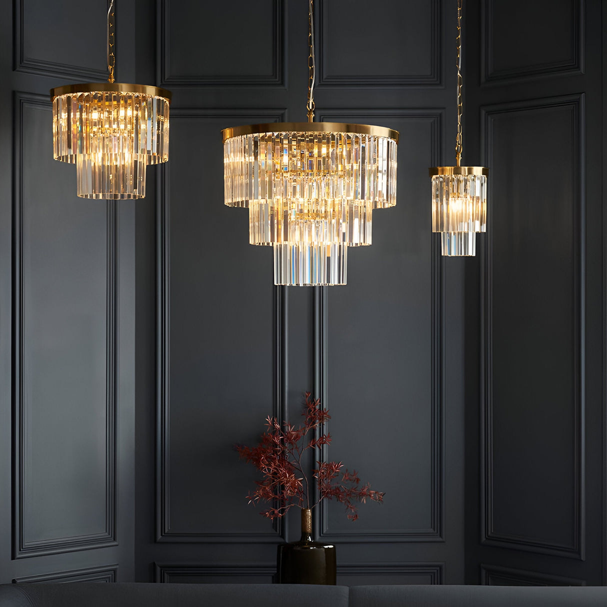 Endon Bevstead pendant lights in brushed brass with tiered clear glass lozenge drops, shown in three sizes against a dark panelled wall.