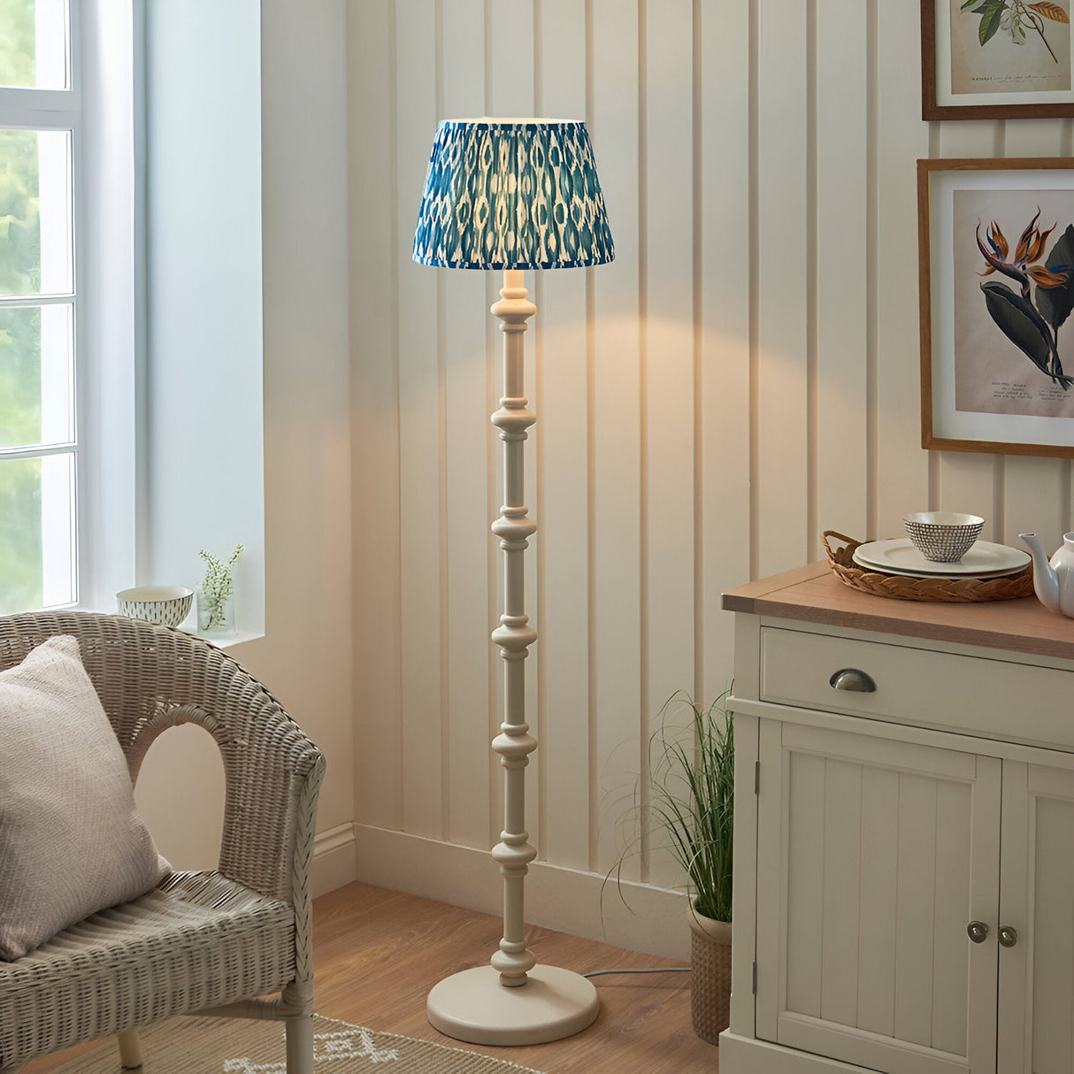 Endon Bevbury Ikat floor lamp with turned white wooden spindle base and blue patterned pleated shade, set in a cream panelled living room corner.
