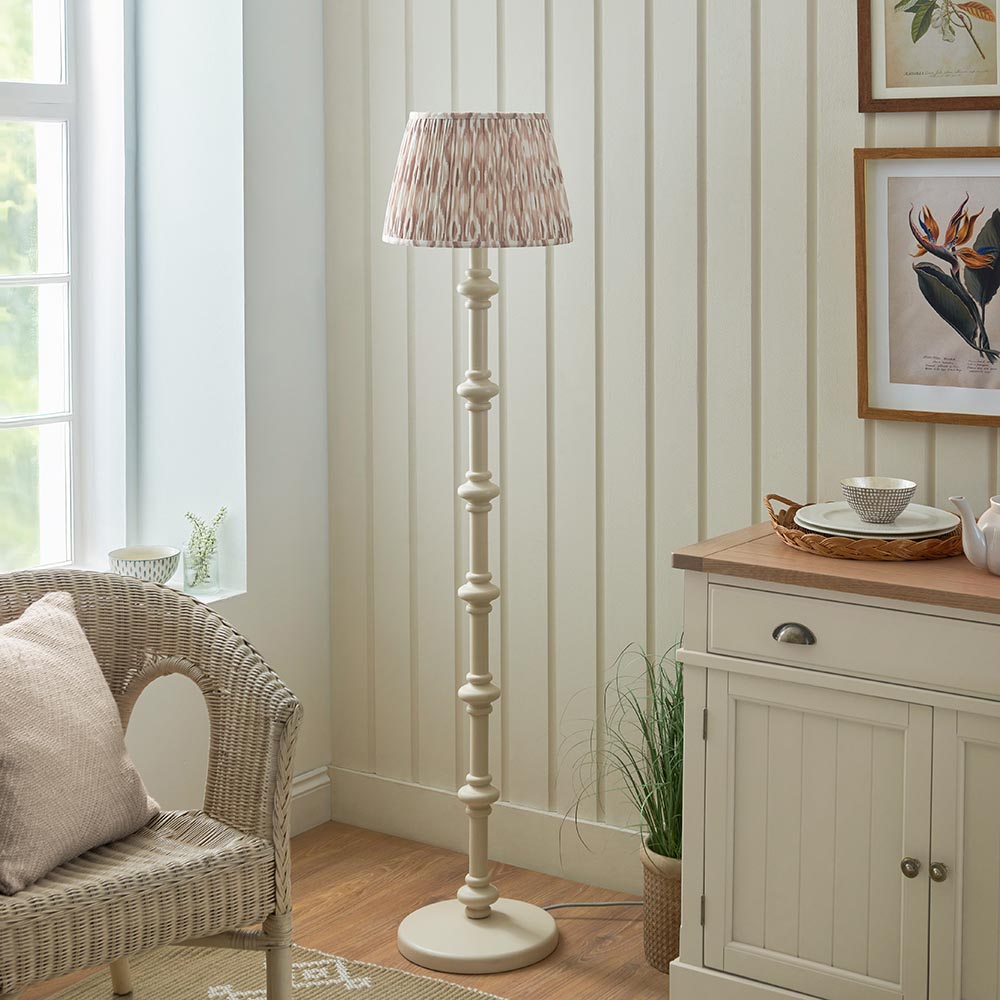 Bevbury Ikat Floor Lamp with turned wooden spindle base in cream, topped with a pleated patterned fabric shade, shown in a living room setting.